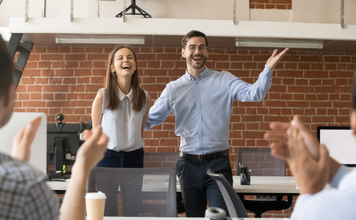 Excited team leader congratulating employee with promotion while team applauding